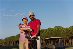 A smiling couple standing with their golf clubs and a golf cart in the background.